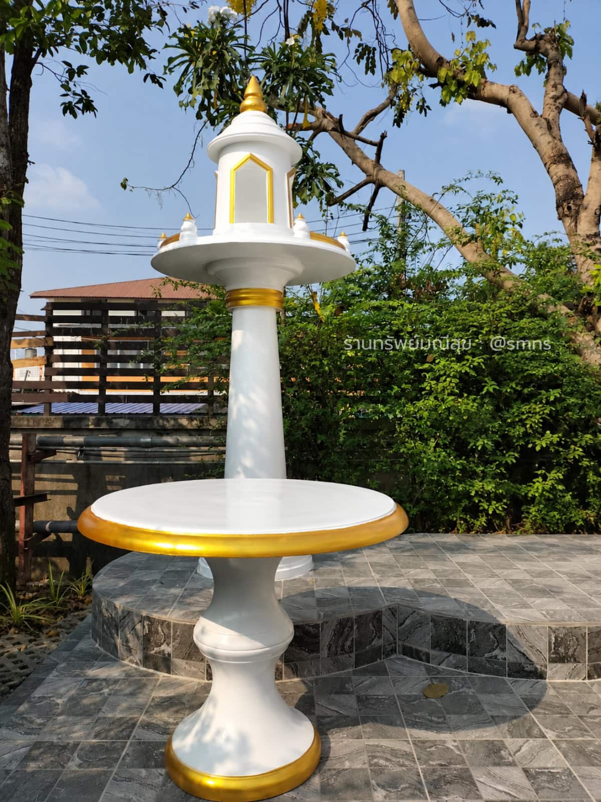 ศาลพระภูมิ MDP-0004 สีขาวตัดทอง พร้อมโต๊ะวางของไหว้ทรงกลม บนพื้นกระเบื้องสีเทาในสวน