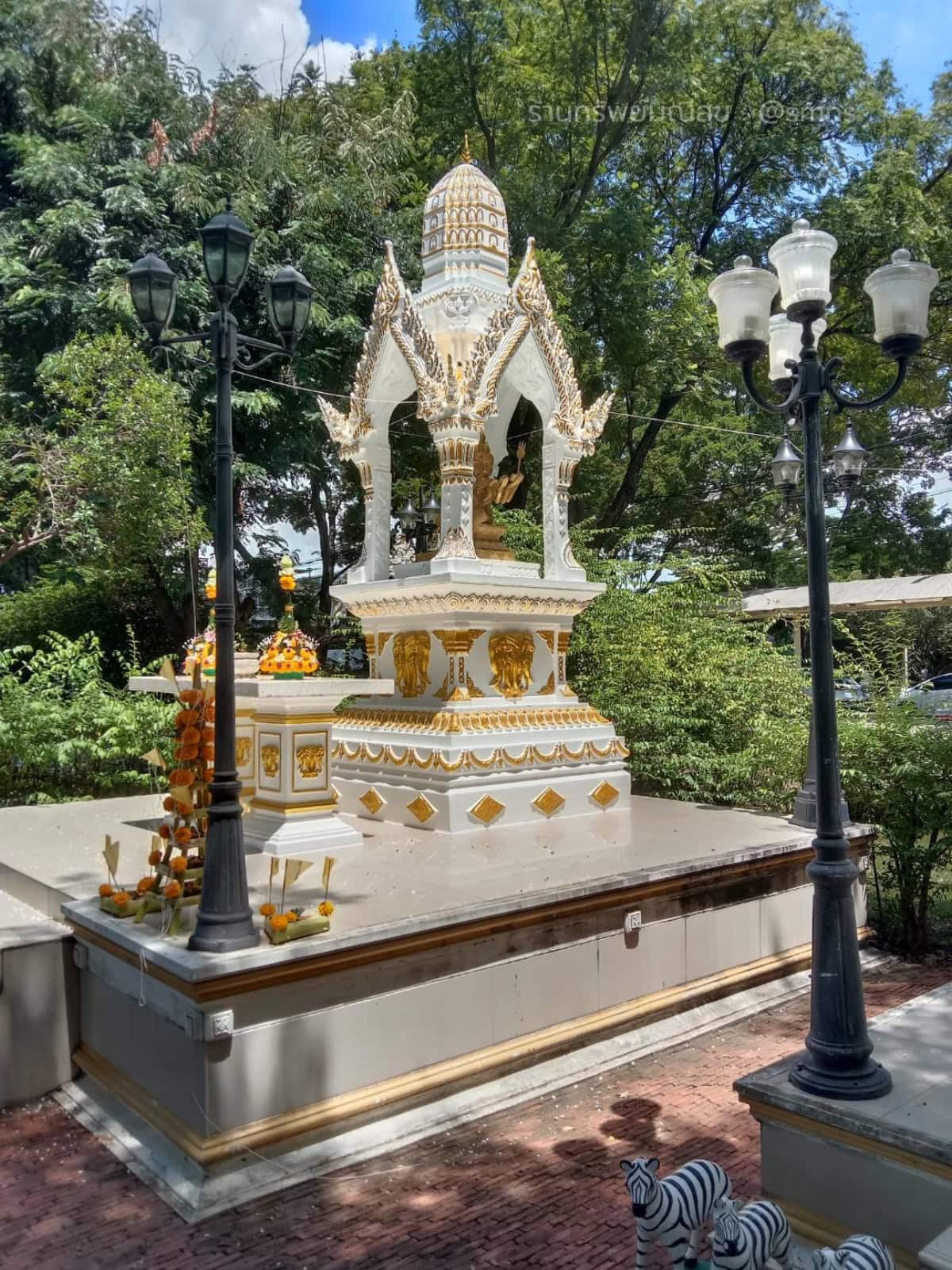 ศาลพระพรหมทรงไทย PST-0020 สีขาวตัดทอง มุมเฉียงในสวน เห็นยอดปรางค์จัมโบ ซุ้มจั่วแหลม และโต๊ะด้านข้าง