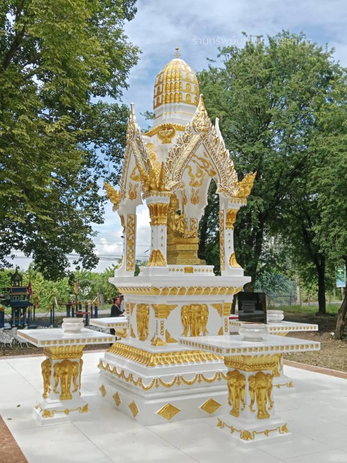 ศาลพระพรหมทรงไทย PST-0020 สีขาวตัดทอง พร้อมโต๊ะวางของไหว้ มุมด้านหน้าในสวนใต้ร่มไม้